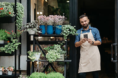 A man standing outside his shop looking at his phone