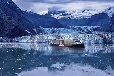 A Celebrity Edge cruise ship in the ocean in front of a glacier and snow-capped mountains.