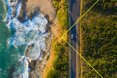 Aerial view of a car driving on a long road by the ocean