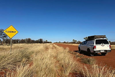 Car travelling along a red dirt road with a floodway sign to the side
