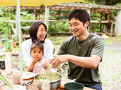 Asian family and friends sitting around a picnic table outside their country house enjoying time together and barbecuing.