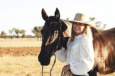 Woman with black horse in field.