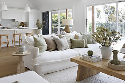 Photo of a living room with a lounge and coffee table and kitchen behind.