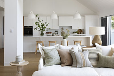 A photo of a white lounge with cushions with a kitchen in the background.