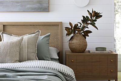 A photo of a bed and a nightstand with a plant.