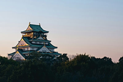 A traditional Japanese castle, peeking over the treetops at dusk