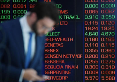 A man checks his phone in front of the ASX board in Sydney. Credit: AAP