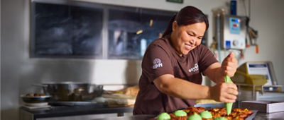 A woman putting green icing on brown cupcakes