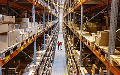 Two people walk down a warehouse aisle with shelves stacked with boxes.