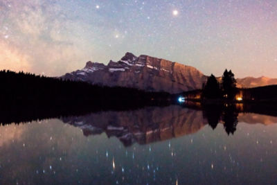 A lake with a mountain behind it and reflected in the water at night time.