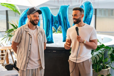 Two men standing infront of a ballon blow-up of letters OMG, man on the right holding a microphone, both men smiling
