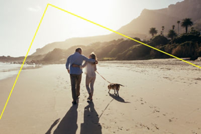 bright low sun over a beach, couple walking with their dog on leash across the sand