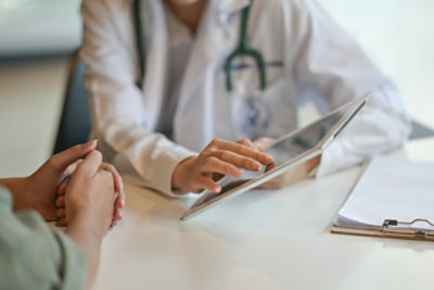 close up of Doctor holding a tablet showing information to a patient who you can see their arms on the left of the image, hands glasp