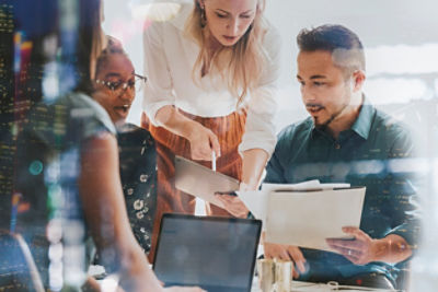 People around a laptop with different papers and tablet looking at project designs
