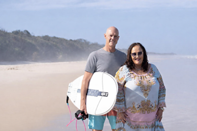 Couple on beach holding surfboard