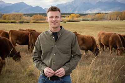 Photo of a man in a open field infront of a few brown cows