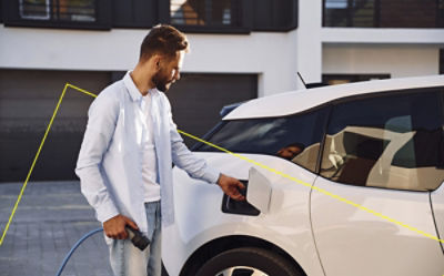 A person in a light blue shirt charging an electric vehicle outside a modern home