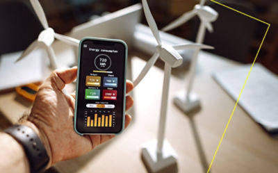 A smartphone displaying an energy consumption dashboard held near a table with model wind turbines.