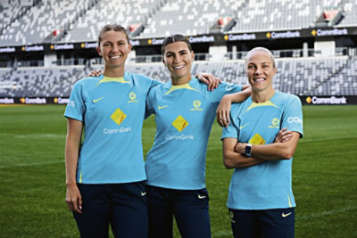 CommBank Matildas Clare Hunt, Steph Catley, and Tameka Yallop standing on a football field in a stadium.