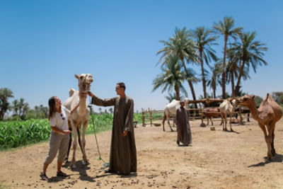 man and woman standing in desert with camel