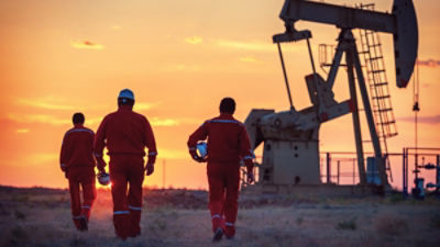 Oilfield workers walking towards a derrick. Credit: Adobe
