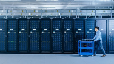 IT technician pushes cart between rows of server racks in a data centre. Picture: Gorodenkoff