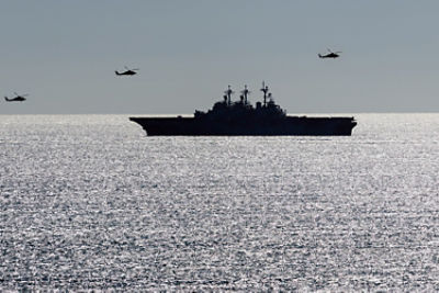 A ship in hormuz with helicopers overhead. Image: Adobe Stock