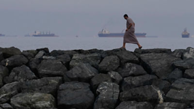 A man walks along the shore as oil tankers and cargo ships line up in the Strait of Hormuz, seen from Khor Fakkan, United Arab Emirates, March 11, 2026. (AP Photo/Altaf Qadri, File)