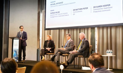 Photo of three people sitting on stage with a fourth standing and speaking for the conference