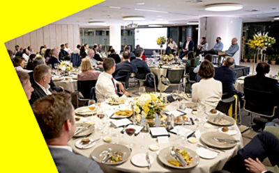Conference room with tables of people and panellists sitting on a stage.