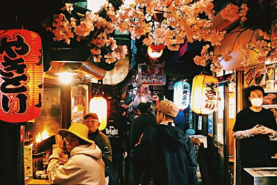A narrow Tokyo alleyway, lined with shops and customers