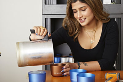 Krish Waje pouring wax into refillable candle containers on a table.